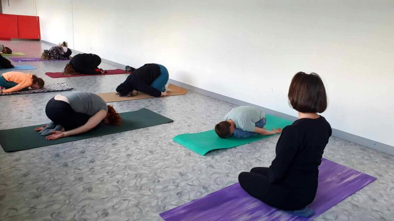 Professeure de yoga sur Ploërmel qui regarde ses élèves faisant le dos rond.